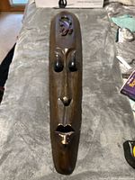 Full view of the entire carved wooden mask on a gray velvet surface showing overall shape and design.