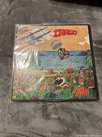 Front cover of Men At Work Cargo vinyl LP showing illustrated tropical scene with biplane and crate.