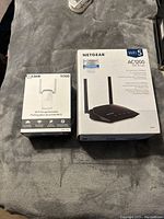 Netgear AC1200 Wi-Fi router box and D-Link N300 Wi-Fi range extender box displayed on surface.