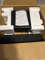 Soundbar system packed in original open box with styrofoam packaging. Remote control and user manual visible on top.
