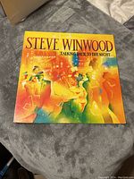 Front cover of the Steve Winwood Talking Back to the Night vinyl LP showing colorful artwork of people and cityscape with the artist and album title.