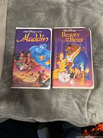 Front view of two VHS tapes, Beauty and the Beast and Aladdin, side by side in their original clamshell cases.