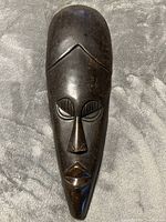 Full front view of the dark brown wooden mask on fabric background.