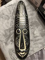 Full view of the wooden mask showing intricate tribal engravings in gold and white on a black base.