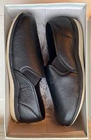 Side view of pair of black men's slippers inside shoebox showing slip-on style and white rubber sole.