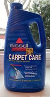 Front view of unopened blue plastic 1.89L Bissell Carpet Care cleaner bottle with handle and label showing product name and use for deep cleaning machines.