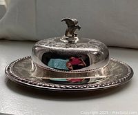 Side angle photo showing copper plated covered butter dish with engraved floral design and bird handle on lid.