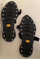 Top view of the pair of Vibram Icers showing the metal studs, rugged rubber tread, and the Vibram logo on each sole.