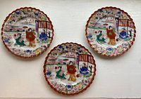 Three scalloped-edged plates with colorful floral and traditional Japanese figure designs placed against a white background, showing overall condition and set quantity.