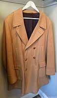 Front view of caramel wool coat with buttons, pockets, and collar on hanger