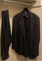 Full view of black Moores men's suit jacket and pants hanging side by side on hangers in a closet, showing overall appearance and fabric texture.