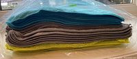 Side view of stacked microfiber cloths showing three distinct colors: blue, grey, and yellow, packed in clear plastic.