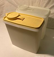 Two vintage Tupperware cereal containers side by side, one with a caramel colored lid and one with a clear lid, shown closed with lids on.