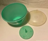 Green round Tupperware container disassembled showing base, green spinner insert, and clear lid on white background.