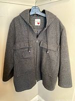Front view of the grey wool coat hanging on a hanger showing hood, zipper, and flap pockets