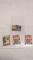 Four 1979 Cracker Jack Superman stamps arranged on a white surface. One smaller stamp shows Superman flying and a classic comic storyline image, three larger stamps show Clark Kent in two versions and a Superman/Roobin pair.