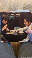 Front cover of John Lennon's 'Nobody Told Me' single showing Lennon and Yoko Ono sitting at a café table.