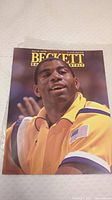 Cover of Beckett Basketball Monthly magazine August 1991 showing Magic Johnson wearing a yellow jacket with American flag patch on the sleeve.