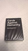 Front of sealed Cards Against Humanity First Expansion box with black cover and white text.