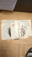 Photo showing a group of 5 vinyl singles in paper sleeves, including Fleetwood Mac and Queen singles.