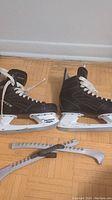 Pair of black 'Spec' ice hockey skates size 9 EE with white laces and white holders marked 'RPM', placed side by side on wooden floor with two gray skate guards in front.