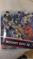 Front cover of the Panini NHL Hockey 2011-12 sticker album showing six NHL players and the NHL logo.