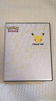 Closed Pokemon card binder with Pikachu face design and 'Train On' text, showing 25th anniversary theme.