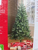 Photo of the artificial tree on packaging showing its full shape and color, along with gift boxes at base.