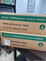 Two cardboard boxes stacked, labeled CMAS Artificial Tree T-12 6FT Wesley Pine.