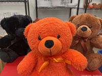 Three sitting teddy bears in orange, brown and black with ribbon bows
