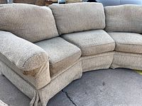 Full side view of the curved sofa with visible arm and cushions showing the fabric texture and shape of the piece.