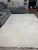 Full view of the ivory faux sheep skin plush rug laid out in front of grey sectional couch.