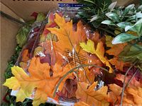 Close-up of artificial autumn leaves including orange and yellow maple leaf shapes and green foliage stems in a box.