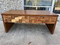Front view of wooden cocktail table showing the geometric pattern drawer fronts and solid legs.