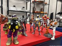 Front view of 10 assorted heroes and villains action figures arranged on red surface, showing details and paintwork