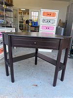 View of diamond-shaped dark wood corner desk showing single front drawer and sturdy legs with lower beam support.