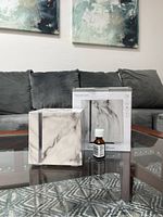 Diffuser displayed alongside its original product box and essential oil bottle on a glass table with a sofa and wall art in the background.