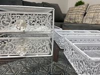 Close-up of small two-drawer metal organizer with decorative filigree and clear knobs showing detail and condition including slight rust on one drawer.