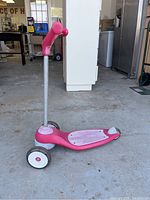 Side view of pink toddler scooter with silver handlebar pole and pink nose cone. Three wheels visible.