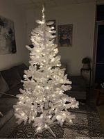 White pre-lit Christmas tree lit with white LED lights in a living room with couch and wall art visible.