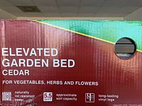 Photo of packaging showing the product name 'Elevated Garden Bed Cedar' and features including natural rot-resistant cedar, 5.5 cubic feet soil capacity, and long-lasting vinyl legs.
