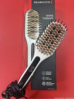 Remington Shine Therapy heat straightening brush on its box with power cord visible. Brush has ceramic-coated bristles and control buttons on handle.