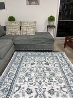 Photo showing the full area rug in front of a gray sectional sofa with patterned pillows, illustrating size and design.