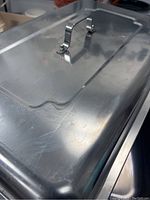 Close-up of the lid showing slightly curved metal handle and surface scratches.