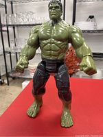 Front view of the 12-inch Incredible Hulk figurine on a red surface, showing muscular build, facial expression, and clothing details.