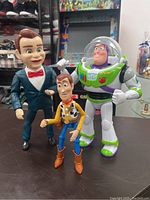 Photo showing all three figurines standing on table including Buzz Lightyear, Woody, and ventriloquist dummy figure