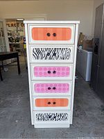 Front view of tall white dresser with colorful drawer fronts in orange, pink, and zebra prints.