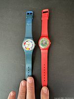 Pair of men's vintage Swatch watches, one with blue strap and signal flags dial, one with red strap and colorful design dial.