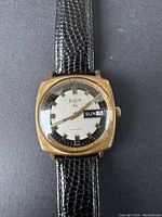 Front view of vintage Elgin automatic men's wristwatch showing square brass-tone case, silver dial, day-date window, and black textured leather strap.