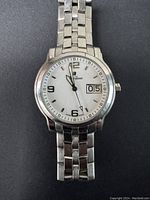 Front and close-up view of the watch showing white dial, hour markers, hands, date window, and metal bracelet.